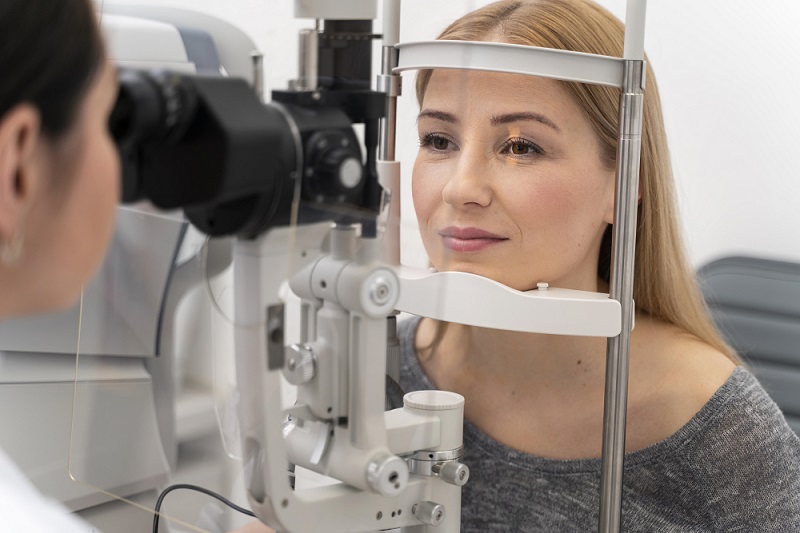 mulher está em frente a um aparelho de verificação de acuidade visual durante uma consulta no oftalmologista para saber se precisa de óculos de leitura feminino